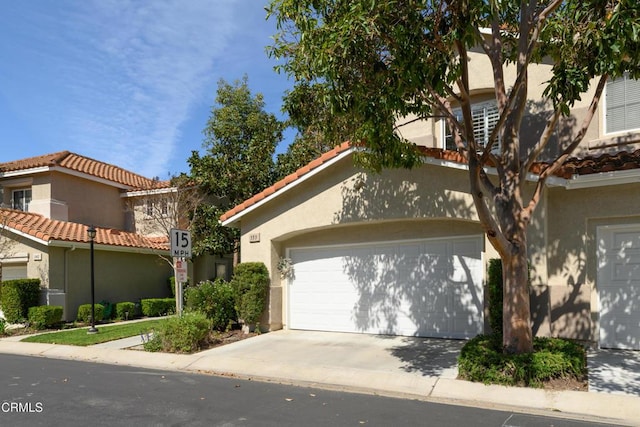 view of front of property with a tiled roof, concrete driveway, stucco siding, and an attached garage