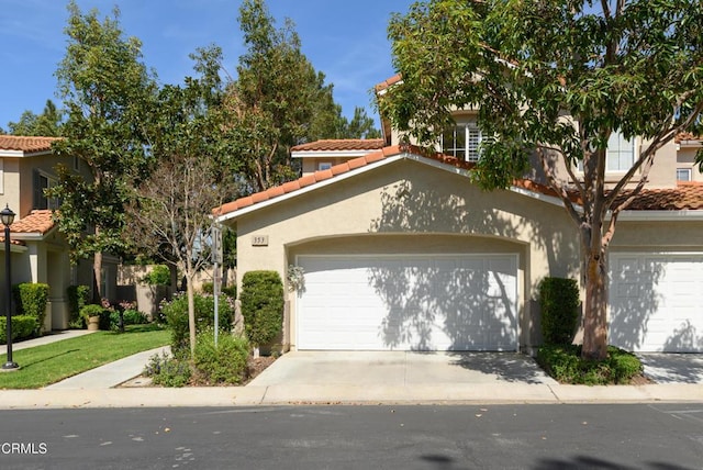 mediterranean / spanish house featuring a tile roof, stucco siding, a garage, and driveway