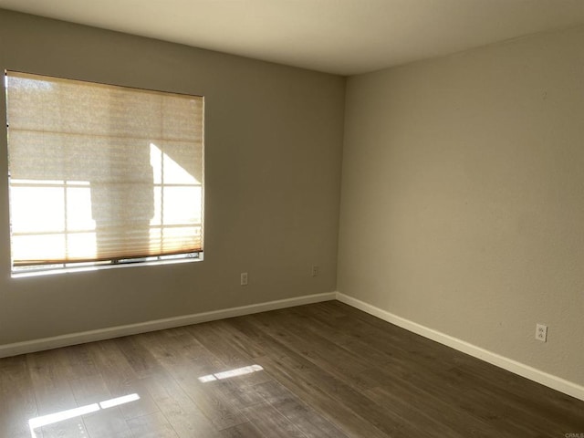 spare room featuring baseboards and dark wood finished floors