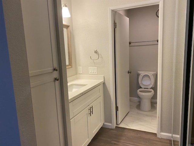 bathroom featuring baseboards, toilet, wood finished floors, and vanity