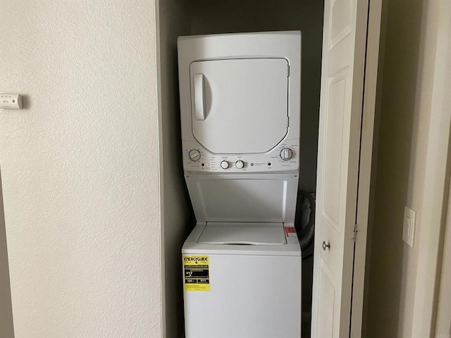 clothes washing area featuring laundry area, stacked washing maching and dryer, and a textured wall