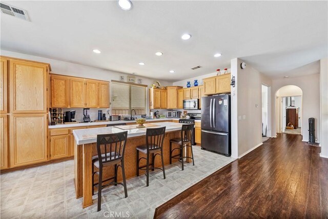 28183 Rocky Cove Dr, Menifee, CA 92585 - kitchen with appliances with stainless steel finishes, arched walkways, a kitchen island, light countertops, and a kitchen breakfast bar