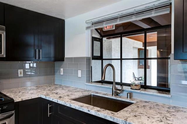 kitchen featuring a sink, light stone counters, and dark cabinetry