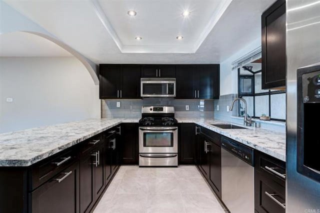 kitchen featuring a sink, stainless steel appliances, arched walkways, a peninsula, and a raised ceiling