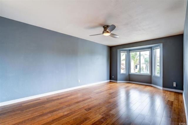 empty room with wood finished floors, baseboards, and ceiling fan