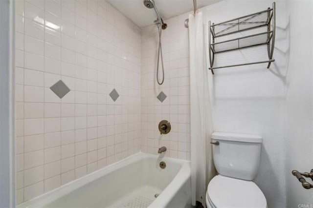 bathroom featuring shower / bathtub combination with curtain and toilet