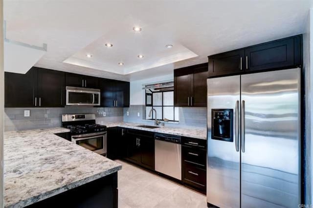 kitchen featuring a sink, stainless steel appliances, a raised ceiling, and decorative backsplash