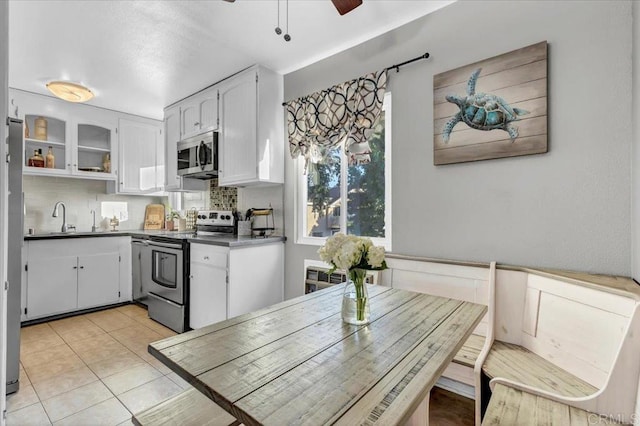 kitchen with dark countertops, ceiling fan, light tile patterned floors, stainless steel appliances, and white cabinetry