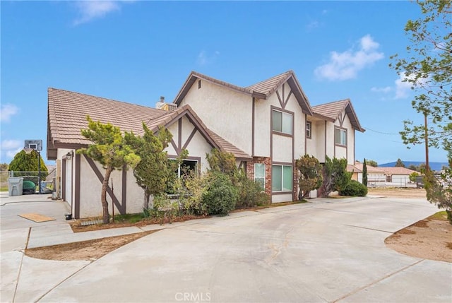 tudor-style house with a tile roof, driveway, and stucco siding