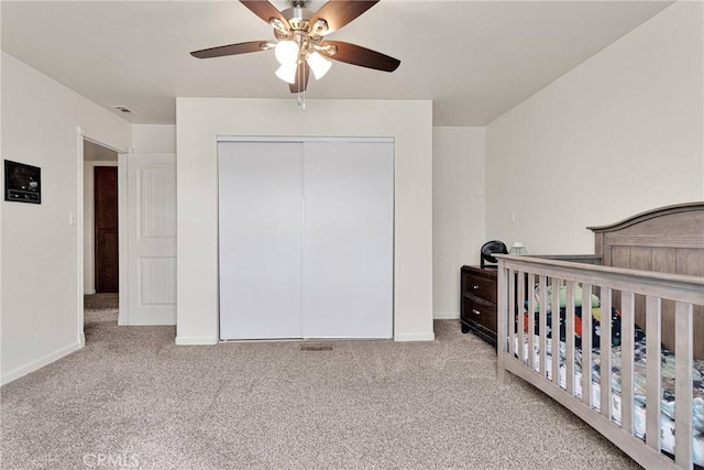 carpeted bedroom with visible vents, a crib, baseboards, a closet, and a ceiling fan