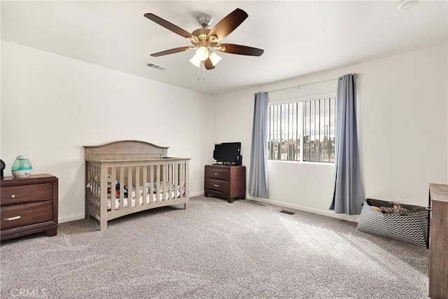 carpeted bedroom with visible vents, baseboards, a nursery area, and ceiling fan