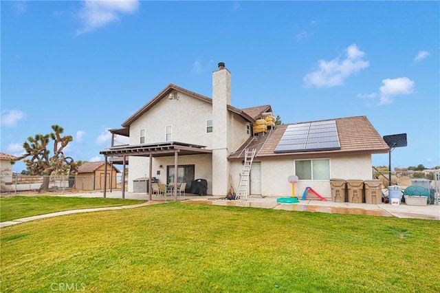 rear view of house featuring stucco siding, a patio, roof mounted solar panels, and a yard