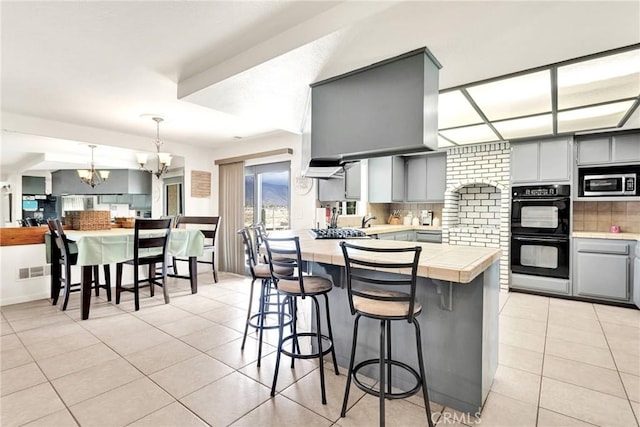 kitchen featuring gray cabinetry, a chandelier, light tile patterned floors, appliances with stainless steel finishes, and a peninsula