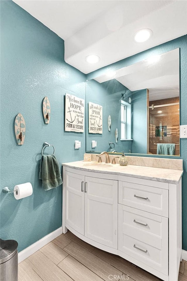 bathroom with a shower with shower door, baseboards, wood finished floors, and vanity