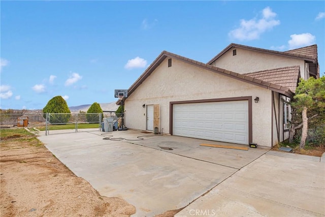 view of side of property with stucco siding, concrete driveway, a garage, and a gate