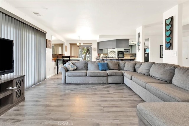 living room featuring visible vents, light wood-type flooring, and an inviting chandelier