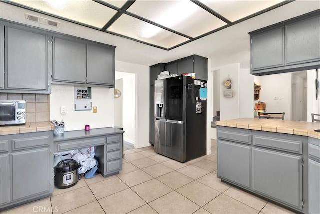 kitchen featuring visible vents, gray cabinetry, tile counters, decorative backsplash, and black fridge with ice dispenser