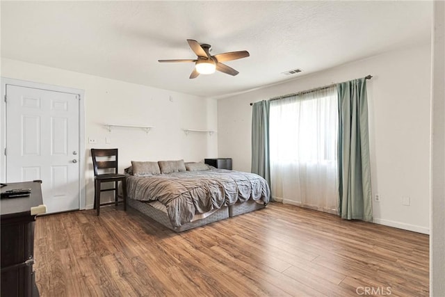 bedroom with visible vents, a ceiling fan, baseboards, and wood finished floors