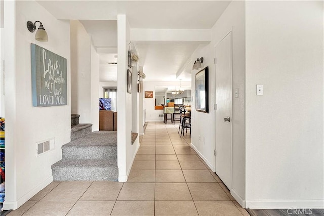 hallway featuring stairway, light tile patterned floors, baseboards, visible vents, and an inviting chandelier