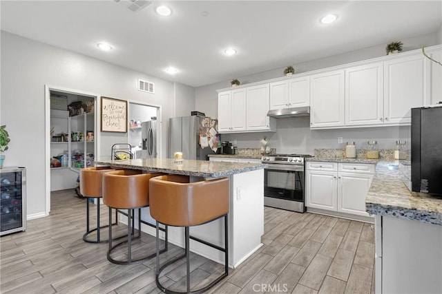 kitchen with under cabinet range hood, wine cooler, appliances with stainless steel finishes, and wood tiled floor