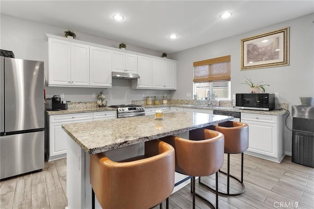 kitchen featuring under cabinet range hood, wood finish floors, appliances with stainless steel finishes, and a kitchen island