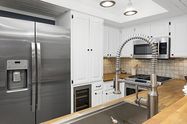 kitchen featuring beverage cooler, butcher block countertops, decorative backsplash, white cabinets, and stainless steel appliances