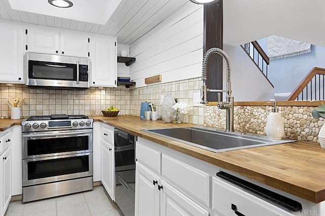 kitchen with light tile patterned flooring, a sink, appliances with stainless steel finishes, wood counters, and tasteful backsplash