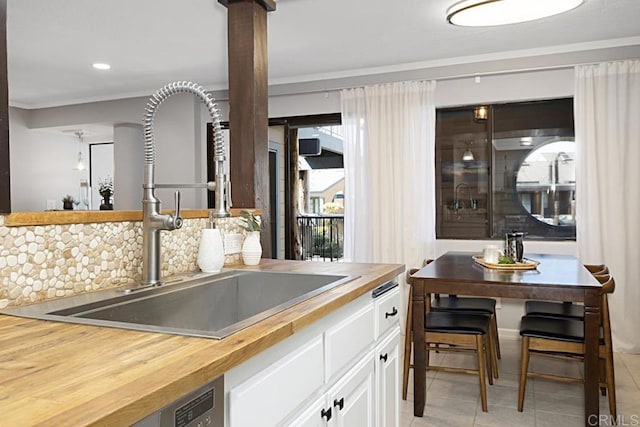 kitchen with butcher block countertops, a sink, tasteful backsplash, light tile patterned flooring, and white cabinets