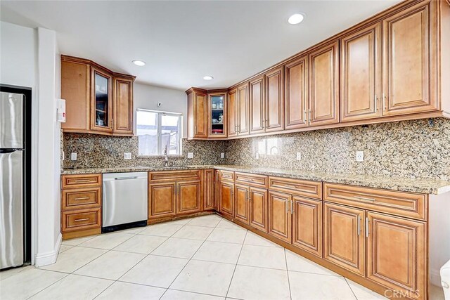 kitchen with brown cabinets, a sink, appliances with stainless steel finishes, light tile patterned flooring, and light stone countertops