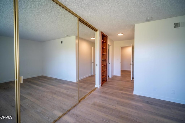 hall featuring visible vents, baseboards, built in features, wood finished floors, and a textured ceiling