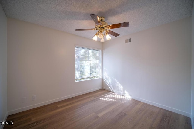 unfurnished room featuring a textured ceiling, wood finished floors, visible vents, and baseboards