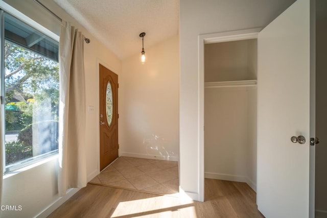 entryway with vaulted ceiling, wood finished floors, baseboards, and a textured ceiling
