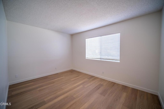 unfurnished room with light wood finished floors, a textured ceiling, and baseboards
