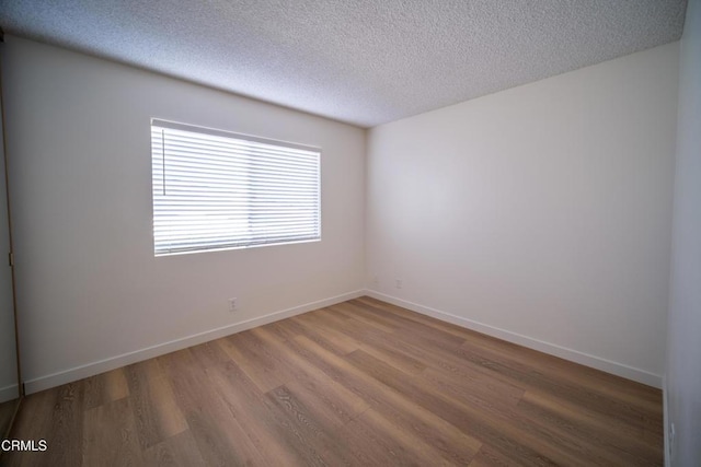 spare room with a textured ceiling, baseboards, and wood finished floors