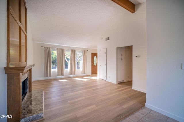 unfurnished living room with light wood-style flooring, beamed ceiling, a high end fireplace, and a textured ceiling