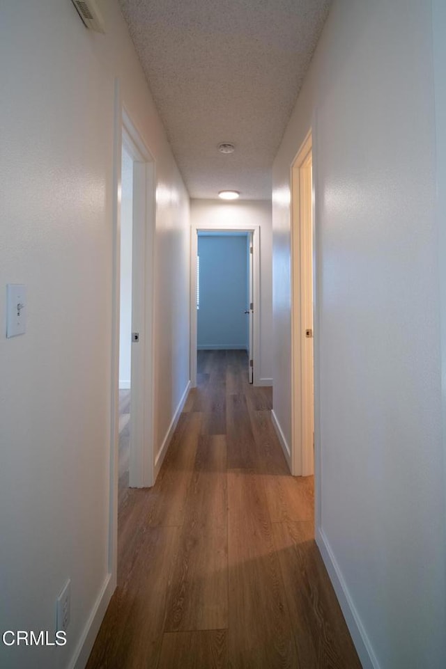 hall with visible vents, baseboards, a textured ceiling, and wood finished floors