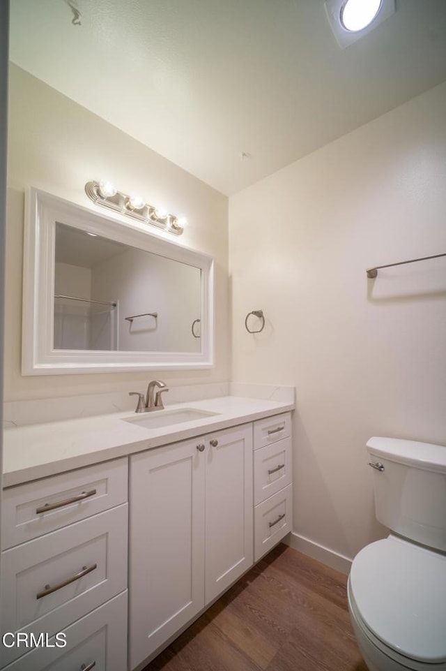 bathroom with baseboards, toilet, wood finished floors, and vanity