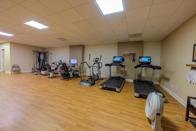 exercise room with light wood finished floors, a paneled ceiling, and baseboards