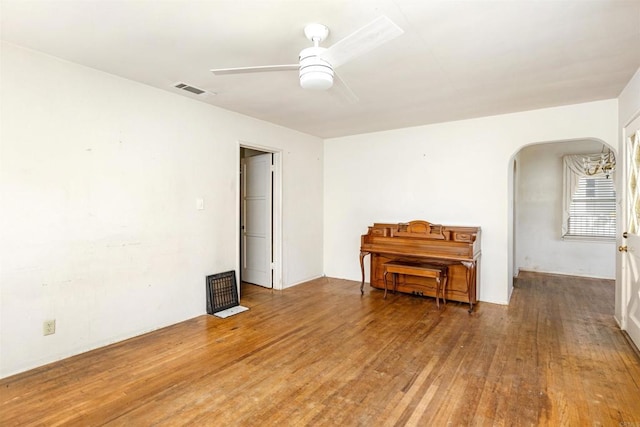 empty room featuring visible vents, arched walkways, hardwood / wood-style floors, and a ceiling fan