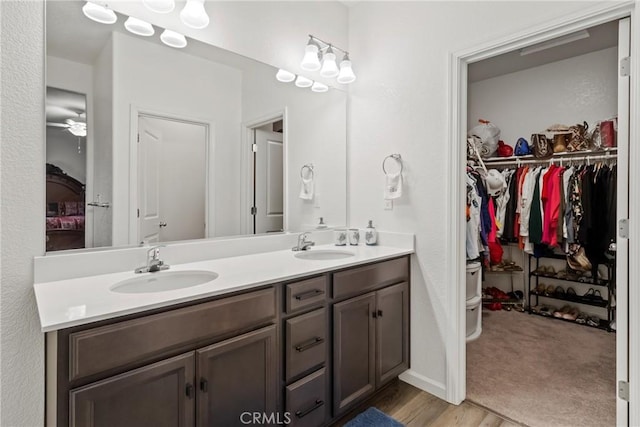 bathroom featuring double vanity, wood finished floors, a walk in closet, and a sink