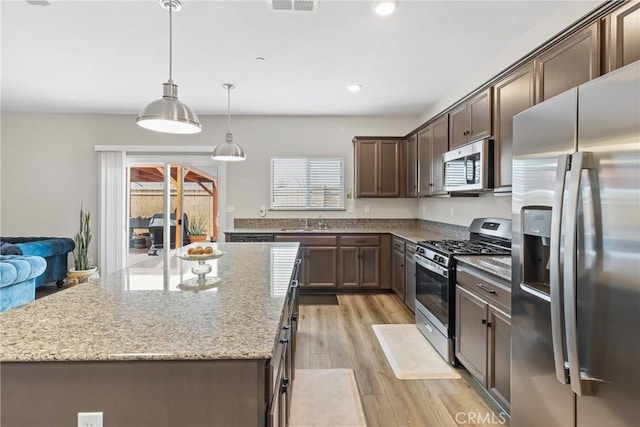 kitchen featuring light stone countertops, a sink, dark brown cabinets, light wood-style floors, and appliances with stainless steel finishes