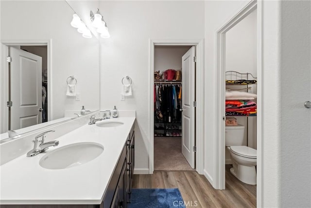 bathroom with toilet, wood finished floors, a walk in closet, and a sink