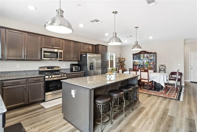 kitchen featuring visible vents, light wood-style flooring, a kitchen island, dark brown cabinetry, and appliances with stainless steel finishes