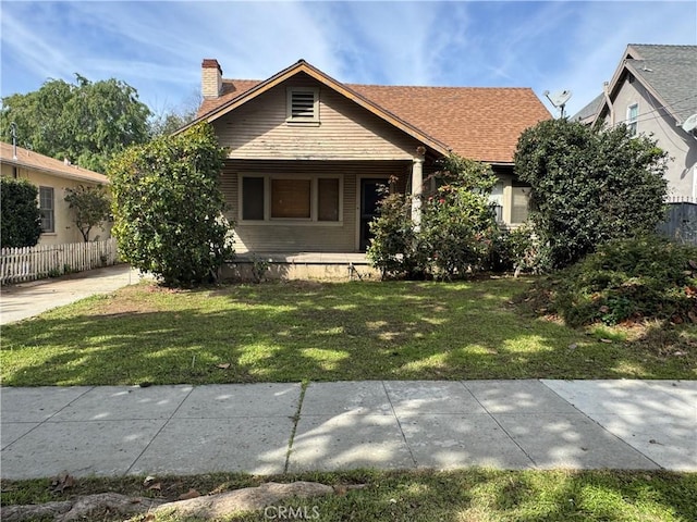 bungalow-style home with a front yard, fence, and a chimney