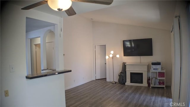 unfurnished living room featuring ceiling fan, wood finished floors, lofted ceiling, a fireplace, and arched walkways