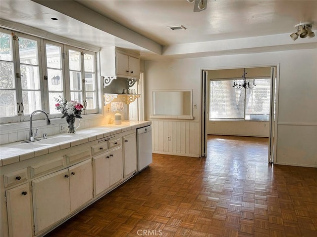kitchen featuring a sink, tile counters, white dishwasher, visible vents, and baseboards
