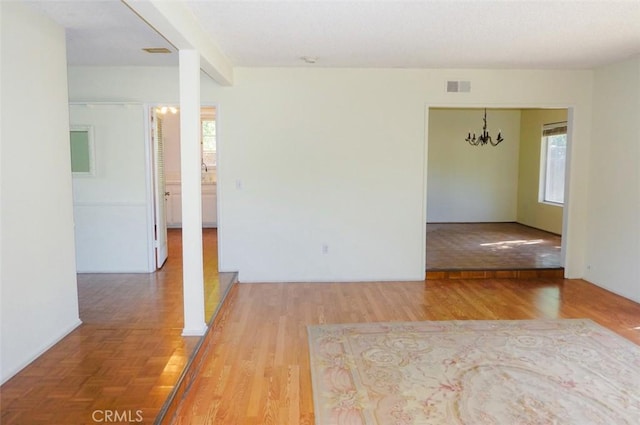 empty room with visible vents, wood finished floors, and a chandelier