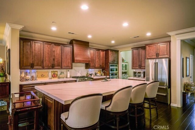 30459 Cowboy Ln, Menifee, CA 92584 - kitchen with appliances with stainless steel finishes, premium range hood, a center island with sink, dark wood-style floors, and crown molding