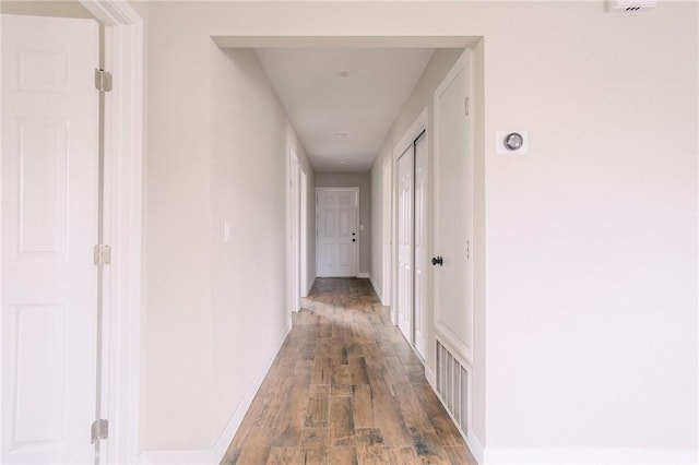 hall featuring visible vents, baseboards, and wood finished floors