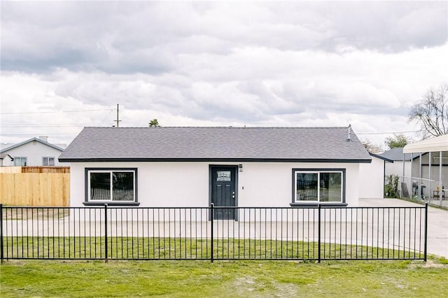 view of front facade featuring stucco siding, fence, a front lawn, and a shingled roof